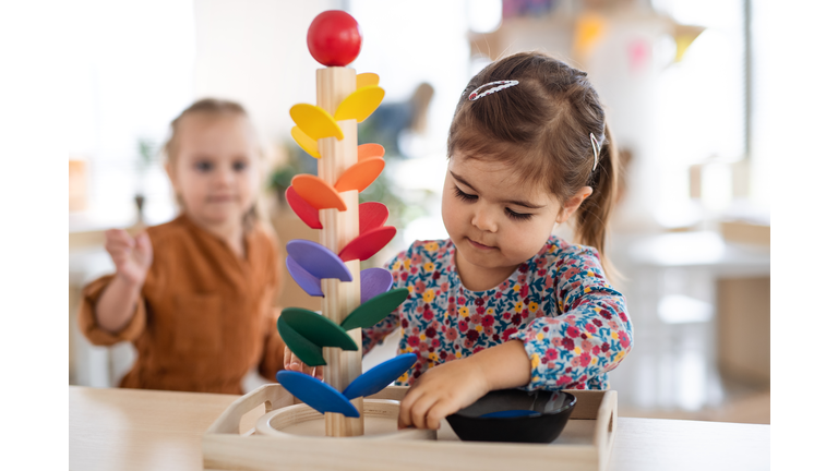 Two pre-school girls playing with marble run indoors in nursery, Montessori education.