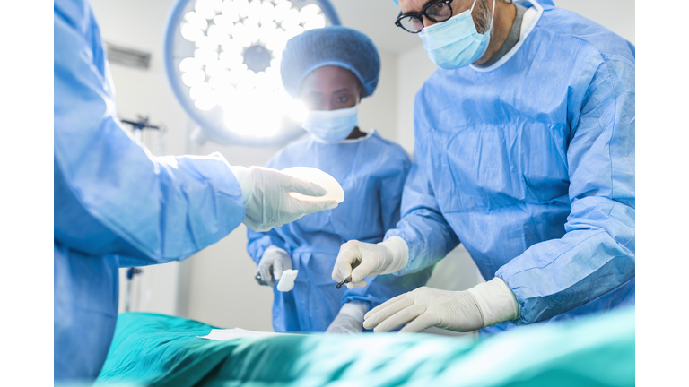 Surgeon and his assistant performing cosmetic surgery in hospital operating room. Surgeon in mask during medical procadure. Breast augmentation, enlargement, enhancement