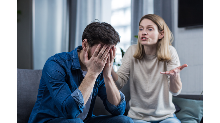 Family conflict, quarrel, misunderstanding. The woman shouts at her husband, in despair, crying. requires explanation. The man listens, covering his face with his hands. Sitting on the couch at home.