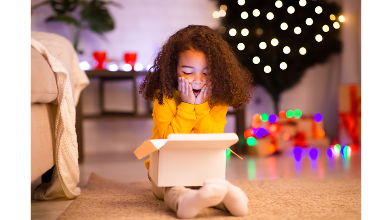Amazed little afro girl opening Christmas gift near xmas tree