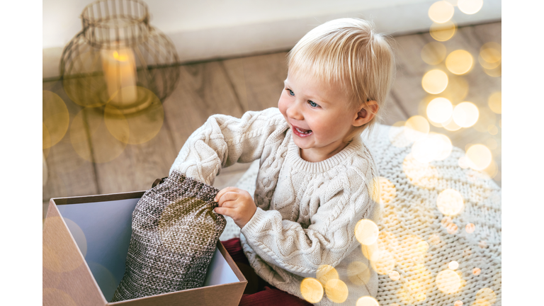 Small laughing baby toddler is opening gift box with smile and joy