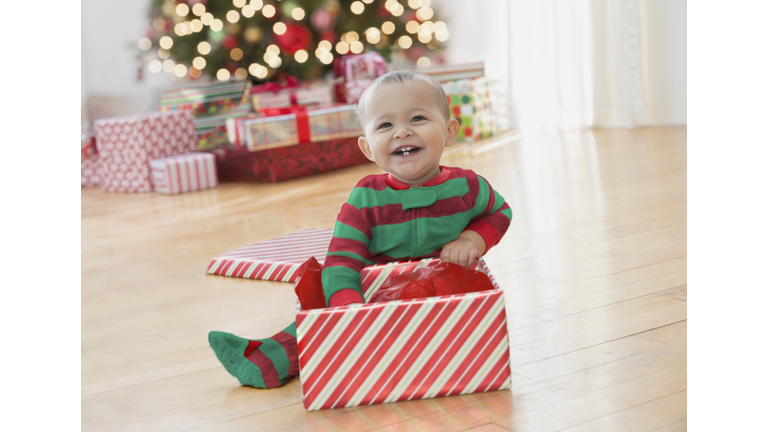 Smiling Mixed Race baby boy sitting on floor playing with Christmas box