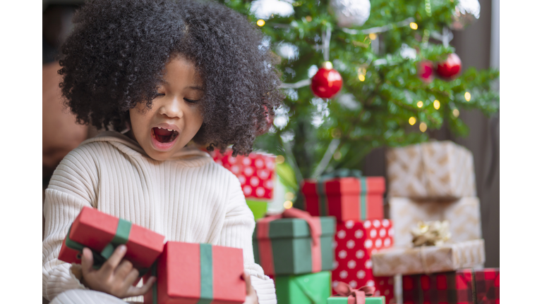 happiness african american child female with afro hair style casual cloth smiling cheerful hand hold christmas present boxes in living room at home