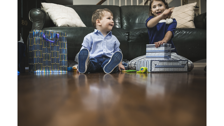 Brother and sister unwrapping Hanukkah gifts in living room at home