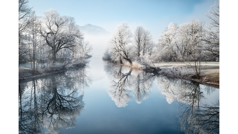Foggy river with snow covered trees with a mountain in the background