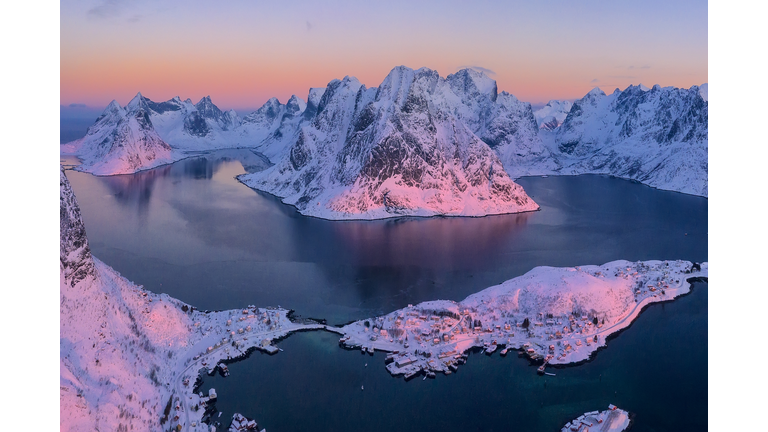 Aerial view of pink sky over snowy peaks and a meandering fjord at sunrise.