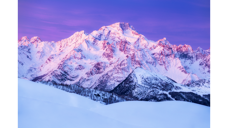 Snowy mountain peaks illuminated by pink light at sunrise.