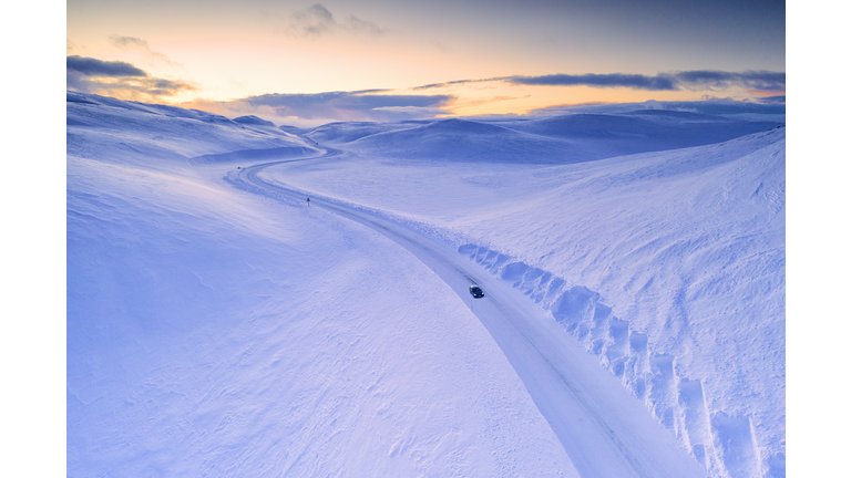 Car traveling on snow covered scenic road at sunset.  