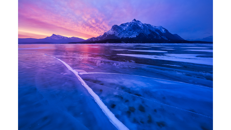 Cracked Ice on frozen glacial lake with a mountain and a dramatic sunset in the background.