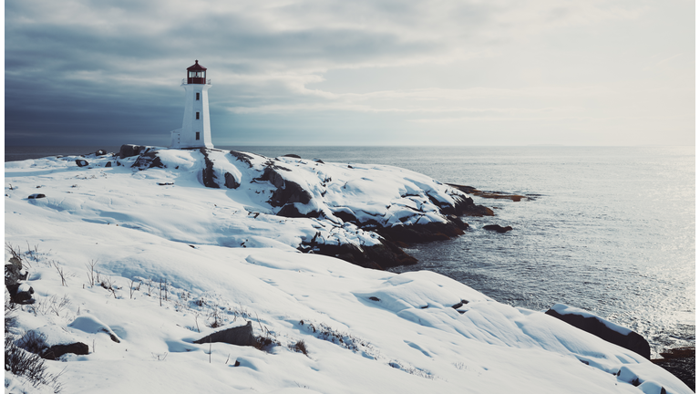 Lighthouse surrounded by snow overlooking the sea.