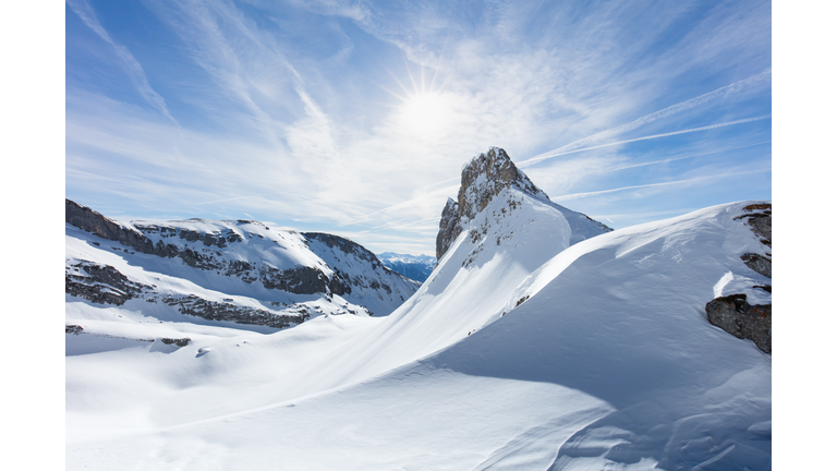 Dramatic clouds behind mountain peaks and slopes covered in snow.