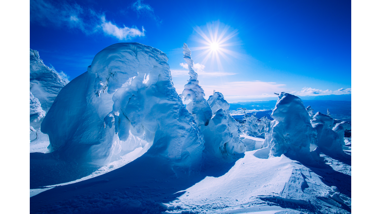 Dramatic snow-covered arch and mountain peaks under a blue sky with bright sunlight.
