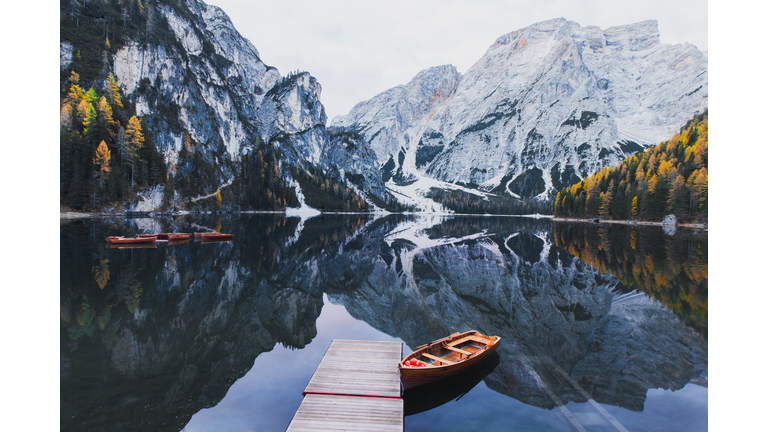 View of a traditional wooden tourist boat on a clear lake reflecting the snow-capped mountain peaks in the background.
