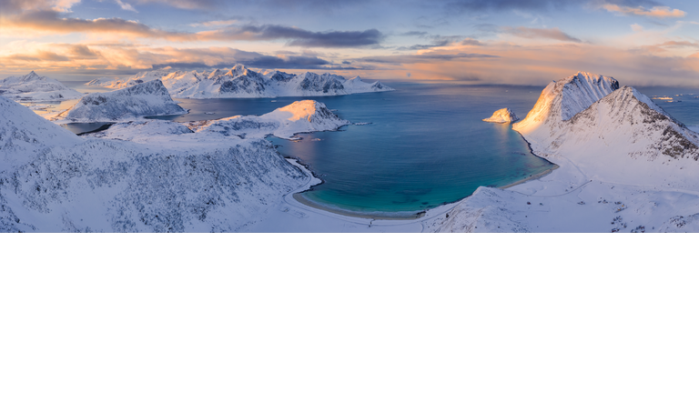 Arial view of a snow covered beach and mountains surrounding a body of water in the center.
