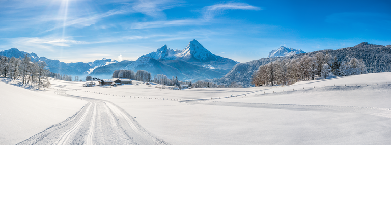 Fresh tracks through snow covered land with mountain peaks and trees in the background.