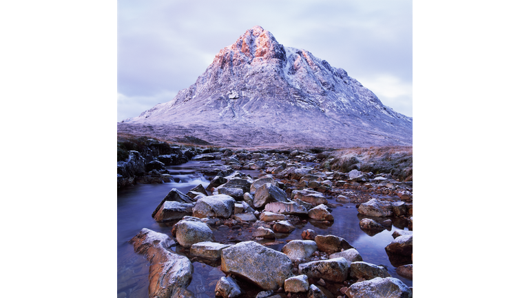 Rocks sticking out of the water in the forefront with a snow capped mountain in the background.