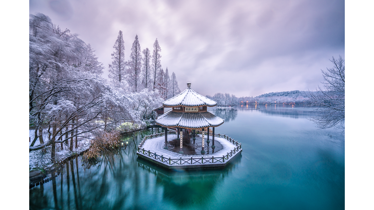 A snow-covered hexagonal structure in the center of a lake surrounded by snow-covered trees.
