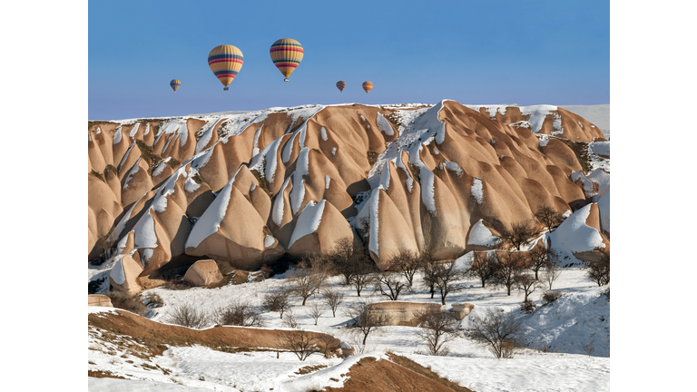 Hot air balloons floating over a spectacular snow-covered rock formations..