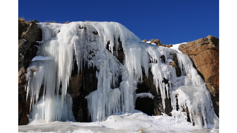 A frozen waterfall that looks like huge icicles hanging from a dark brown mountain.