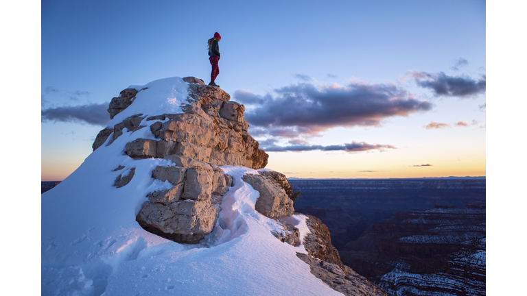 Woman stands on snowy peak at sunset