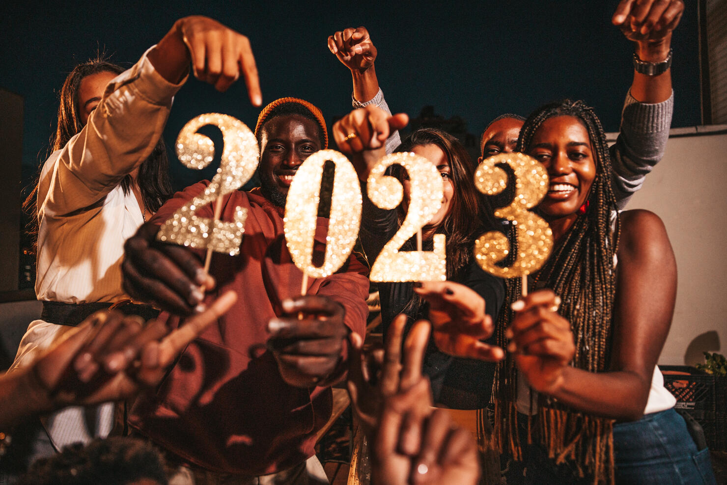 Group of friends celebrating 2023 New Year's Day holding numbers during a rooftop party