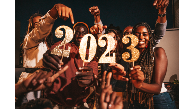 Group of friends celebrating 2023 New Year's Day holding numbers during a rooftop party