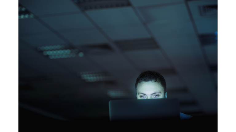 Man looking at laptop computer in office at night