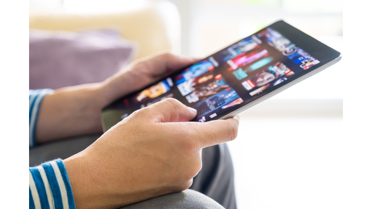 Selective focus at men hand and digital tablet. Young Adult Asian man holding tablet device while choose online movie streaming application with mobile wireless network at home. Entertainment concept.