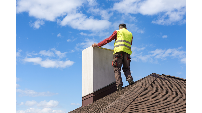 Man measuring chimney on roof top of new house under construction