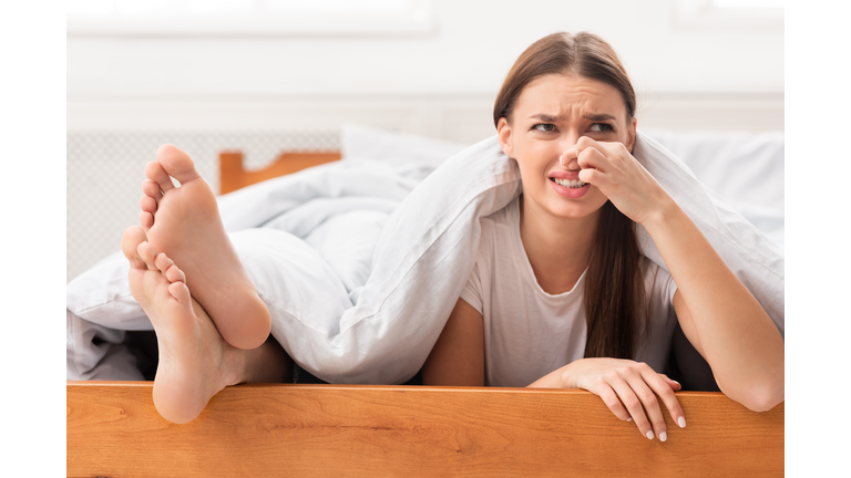 Woman Lying Near Boyfriend's Feet Pinching Nose In Bed Indoor