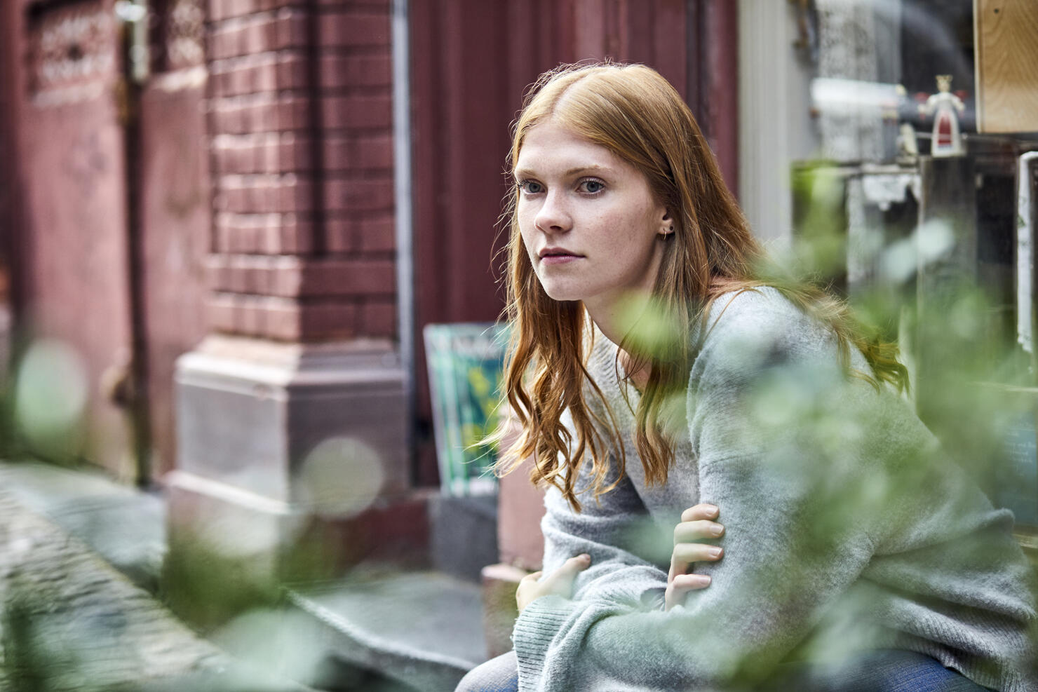 Serious young woman sitting at house entrance