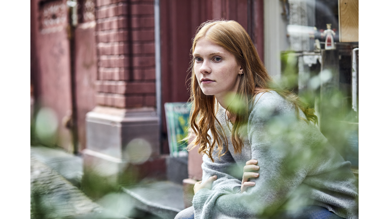 Serious young woman sitting at house entrance