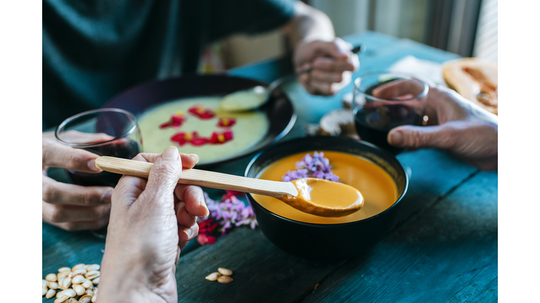 Hand of woman eating creamed pumpkin soup and drinking red wine