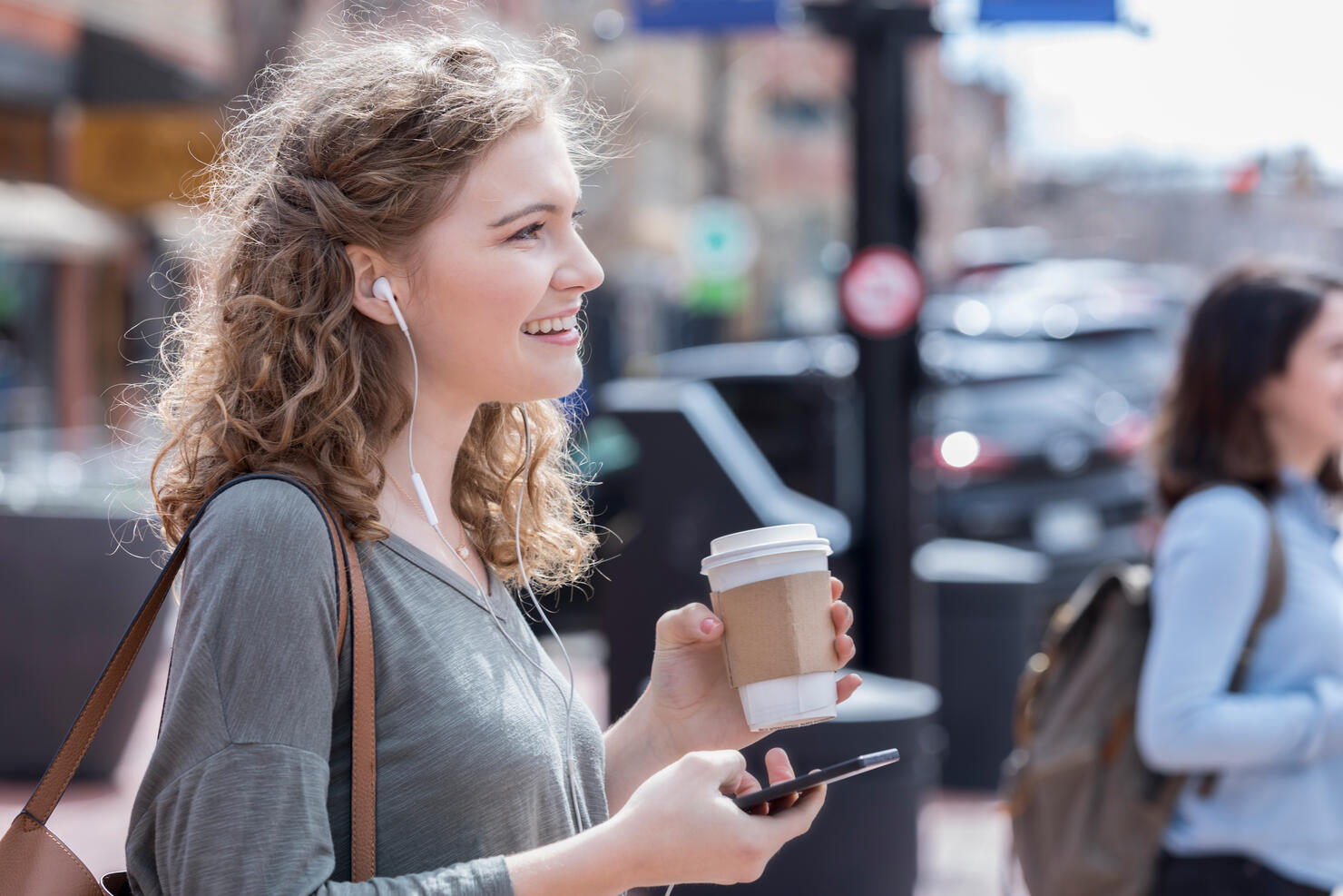 Young woman enjoys music while waiting to cross city street