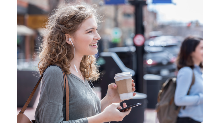 Young woman enjoys music while waiting to cross city street