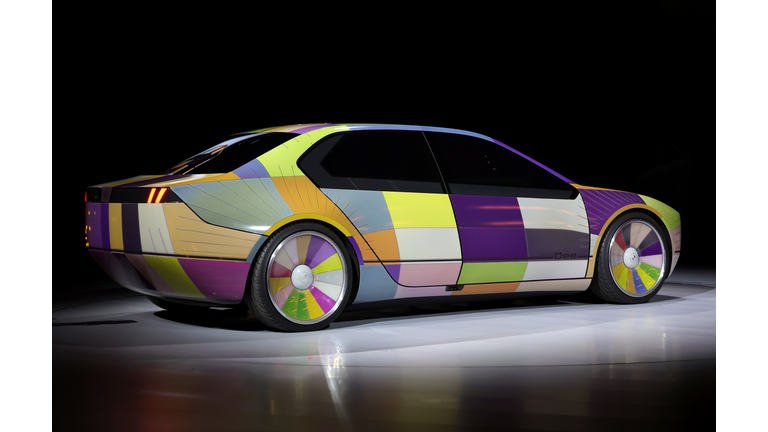 The BMW i Vision Dee concept EV sport sedan displaying multiple colors on it's exterior against a black background.