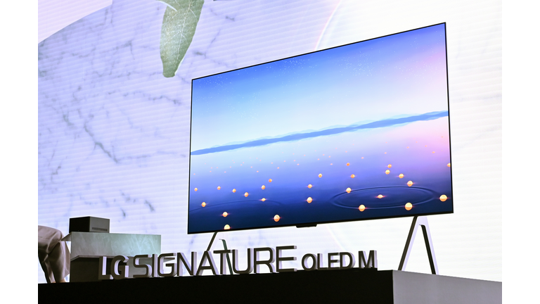 Huge 95-inch flat TV on held up by thin metallic legs on a black display stage.