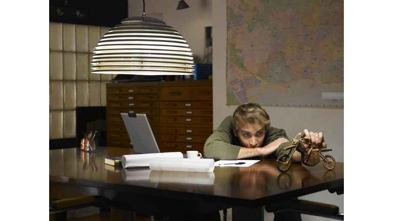 Man playing with model motorcycle at desk in office