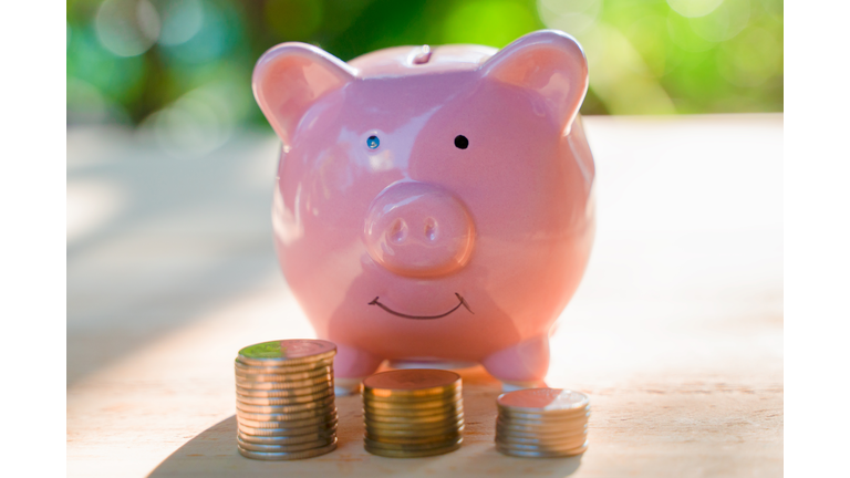 Pink piggy bank with some coins on the brown wooden table with the green background describes the concept of business, finance and money saving