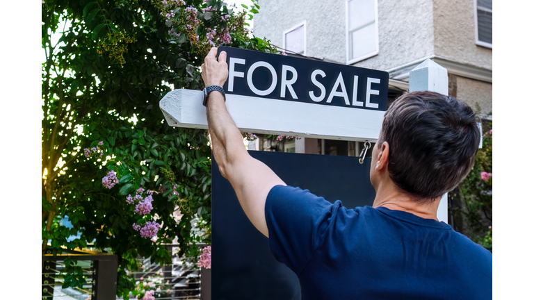 Real Estate Agent Adjusts For Sale Sign in Front Yard