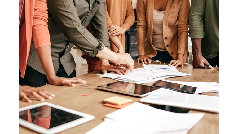 Employees working around a table with papers, pencils, post-it notes, and multiple devices.