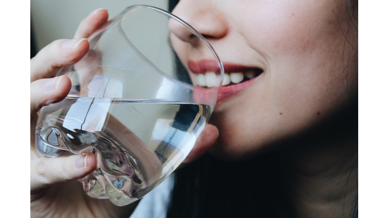 Close-Up Midsection Of Young Woman Drinking Water At Home