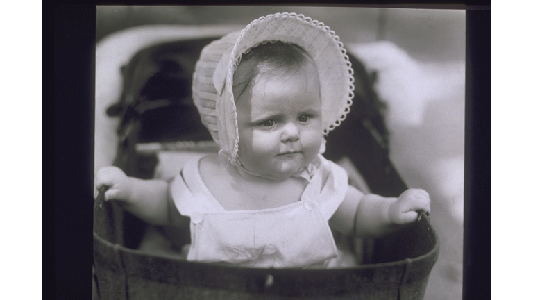 BABY WEARING BONNET IN CARRIAGE, 1940S