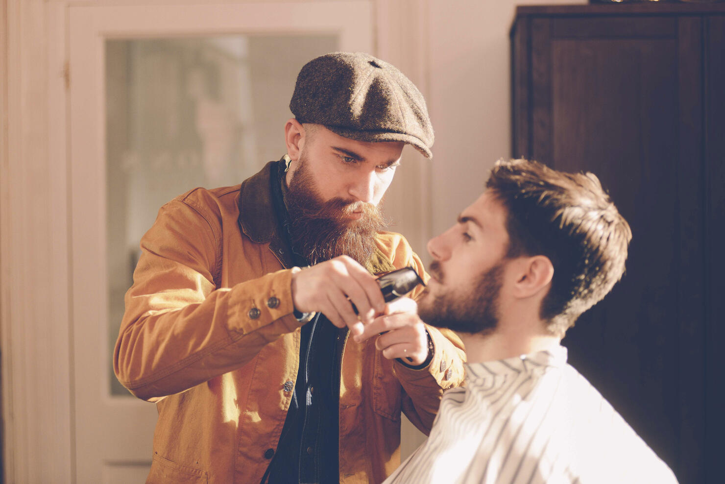 Hip stylist trims customer's beard in barber shop