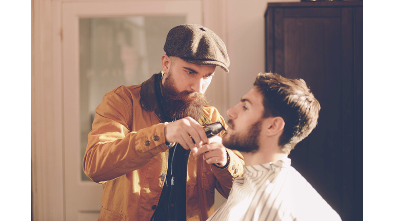 Hip stylist trims customer's beard in barber shop