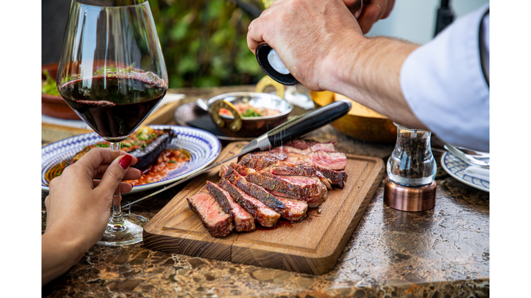 Seasoning medium rare steak with salt grinder, cut on wooden board on restaurant table