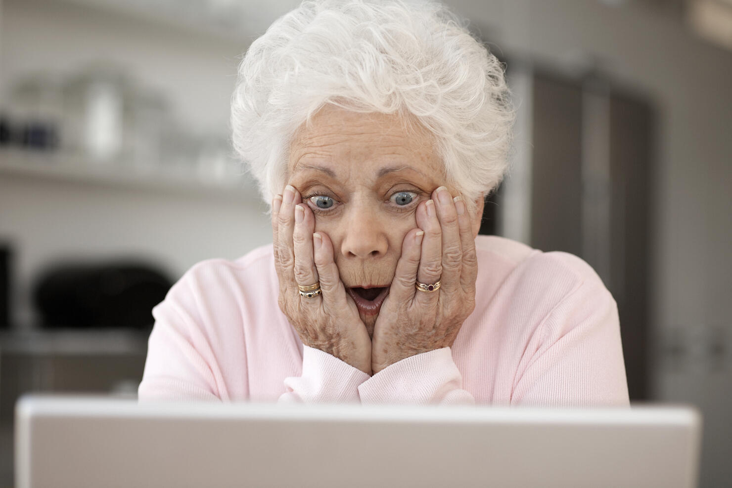 Senior woman looking at laptop with head in hands and open mouth