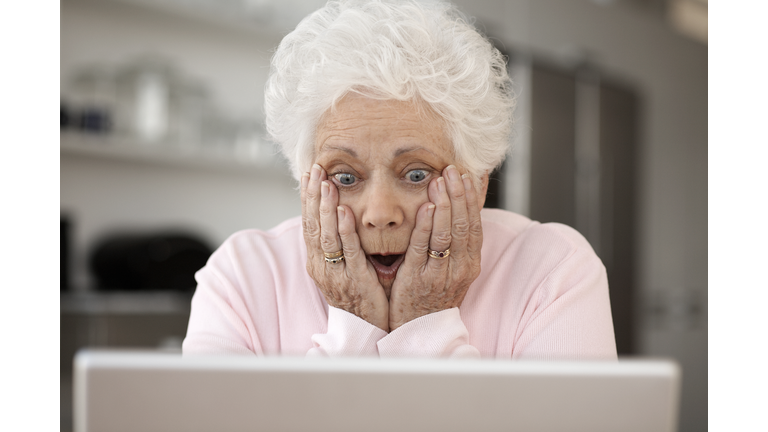 Senior woman looking at laptop with head in hands and open mouth