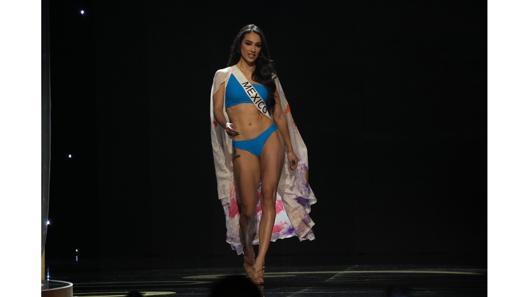 Brunette in blue swimsuit and flowered white cape.
