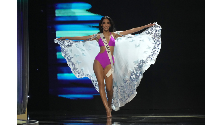 Brunette in lavender swimsuit and white cape.